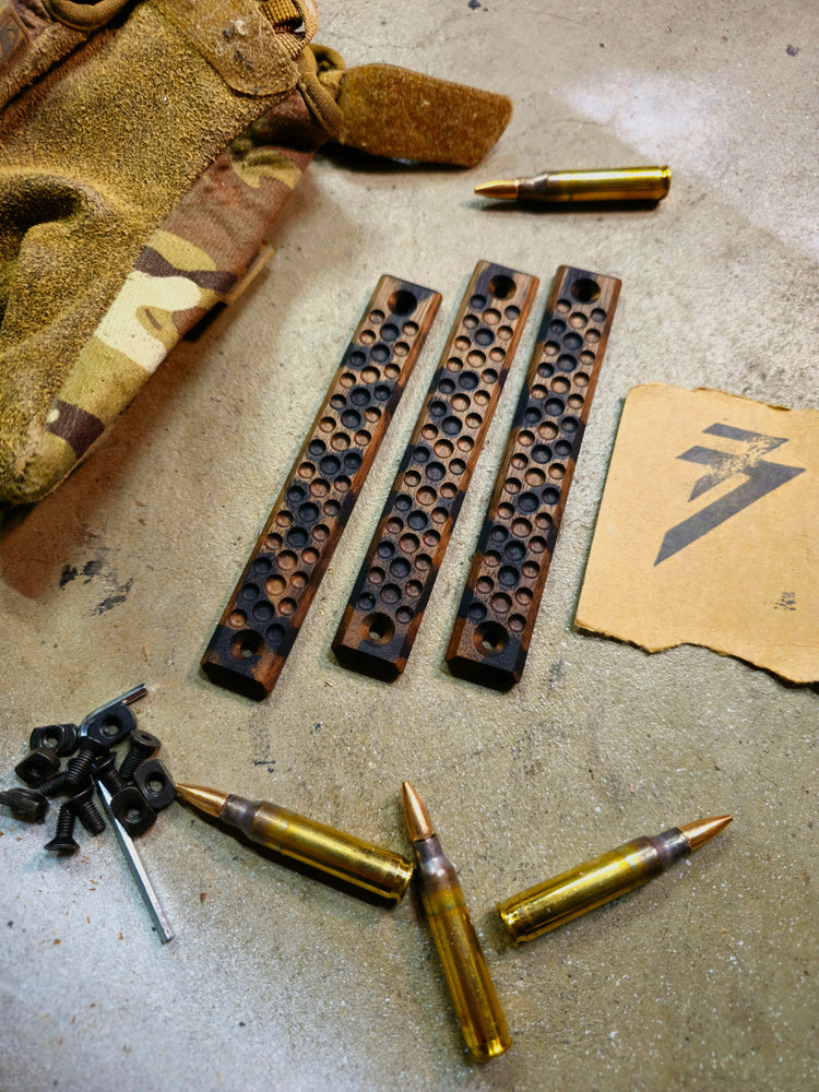 Overhead view of a set of 3 wood mlok rail covers. They are the dimple profile black camo 3 slot rail panel set