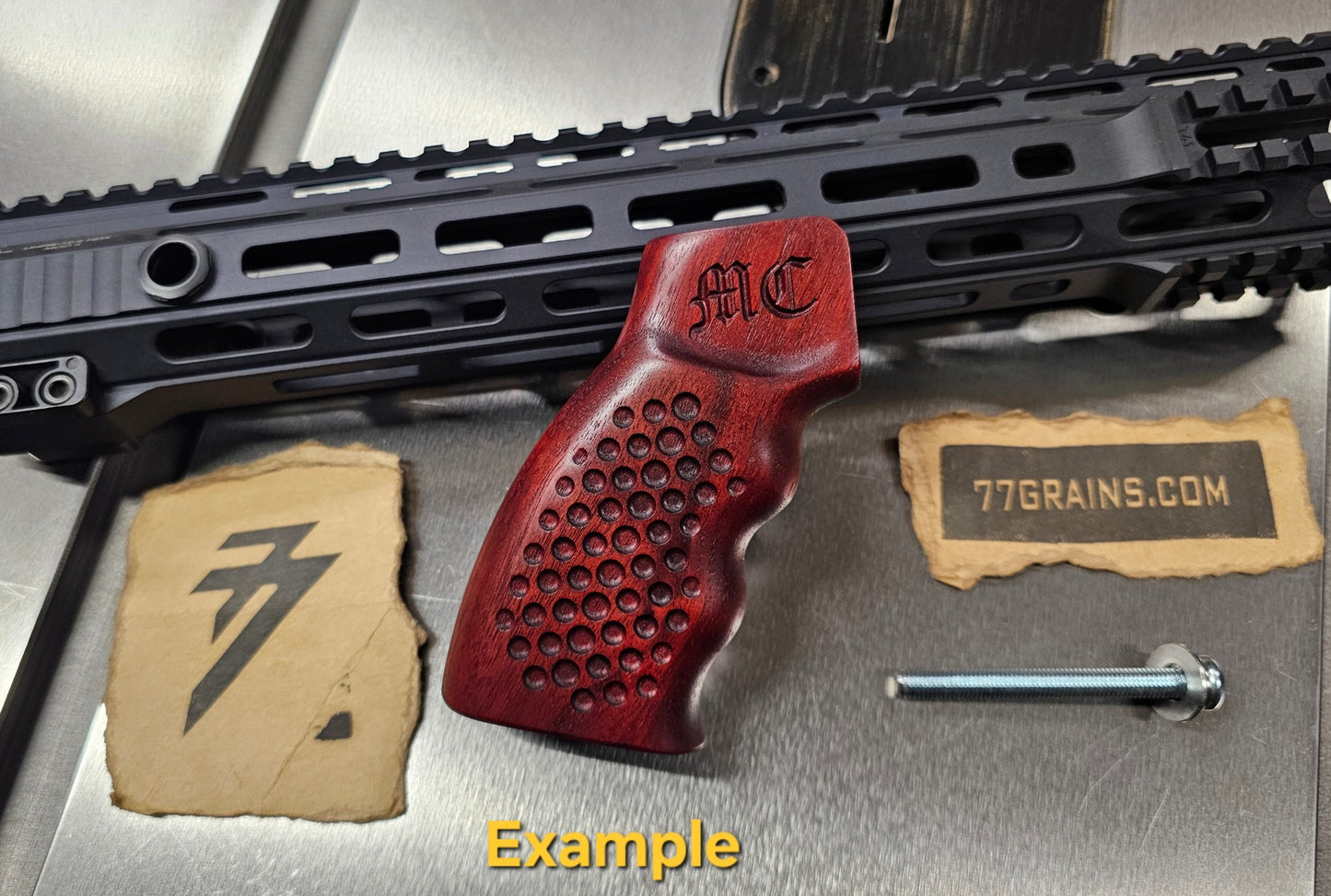 Wooden gun grip with 'MC' branding on a metallic surface with '77Grains.com' label.